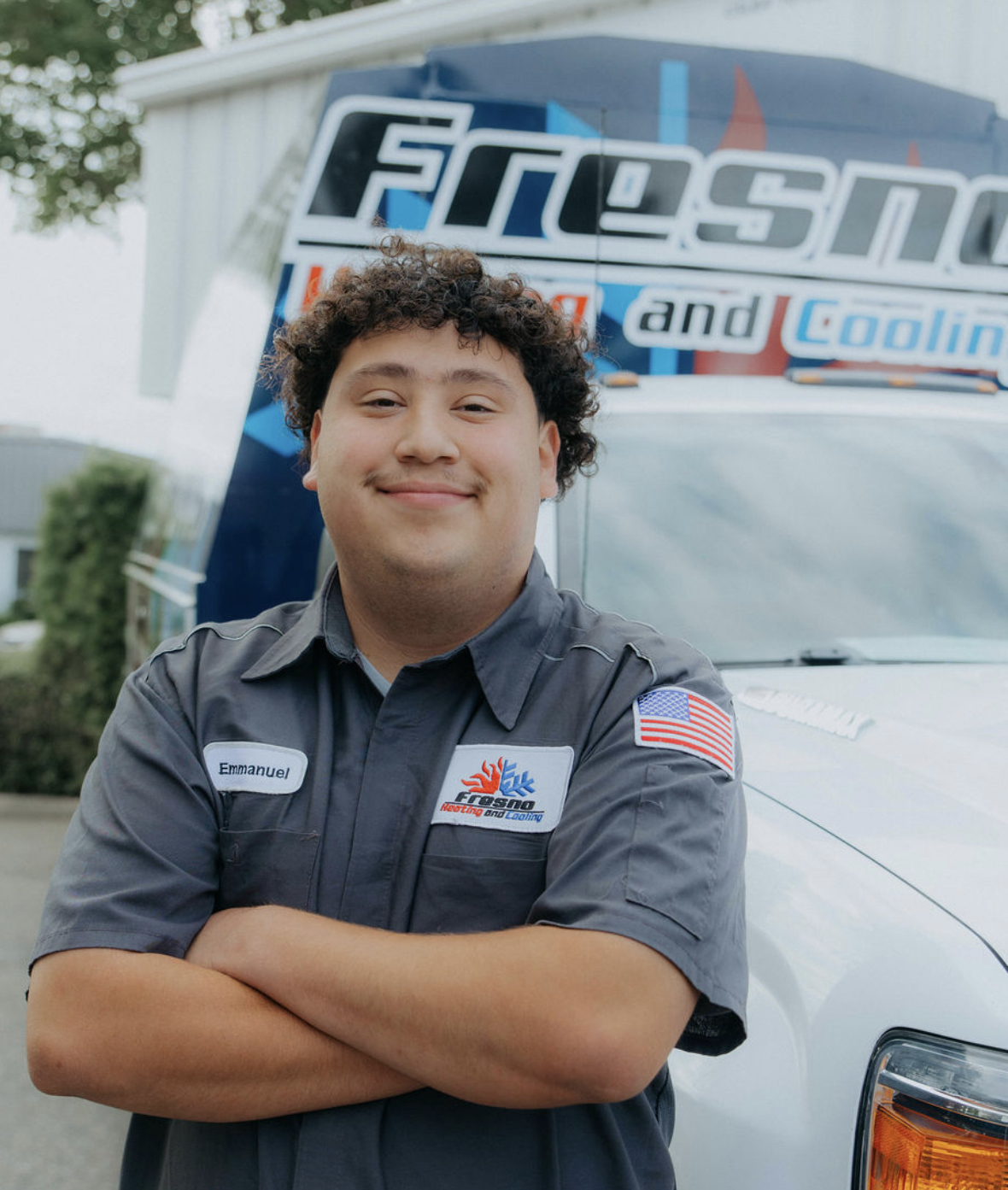 Emmanuel, service technician at Fresno Heating and Cooling, standing with arms crossed in front of a company service truck