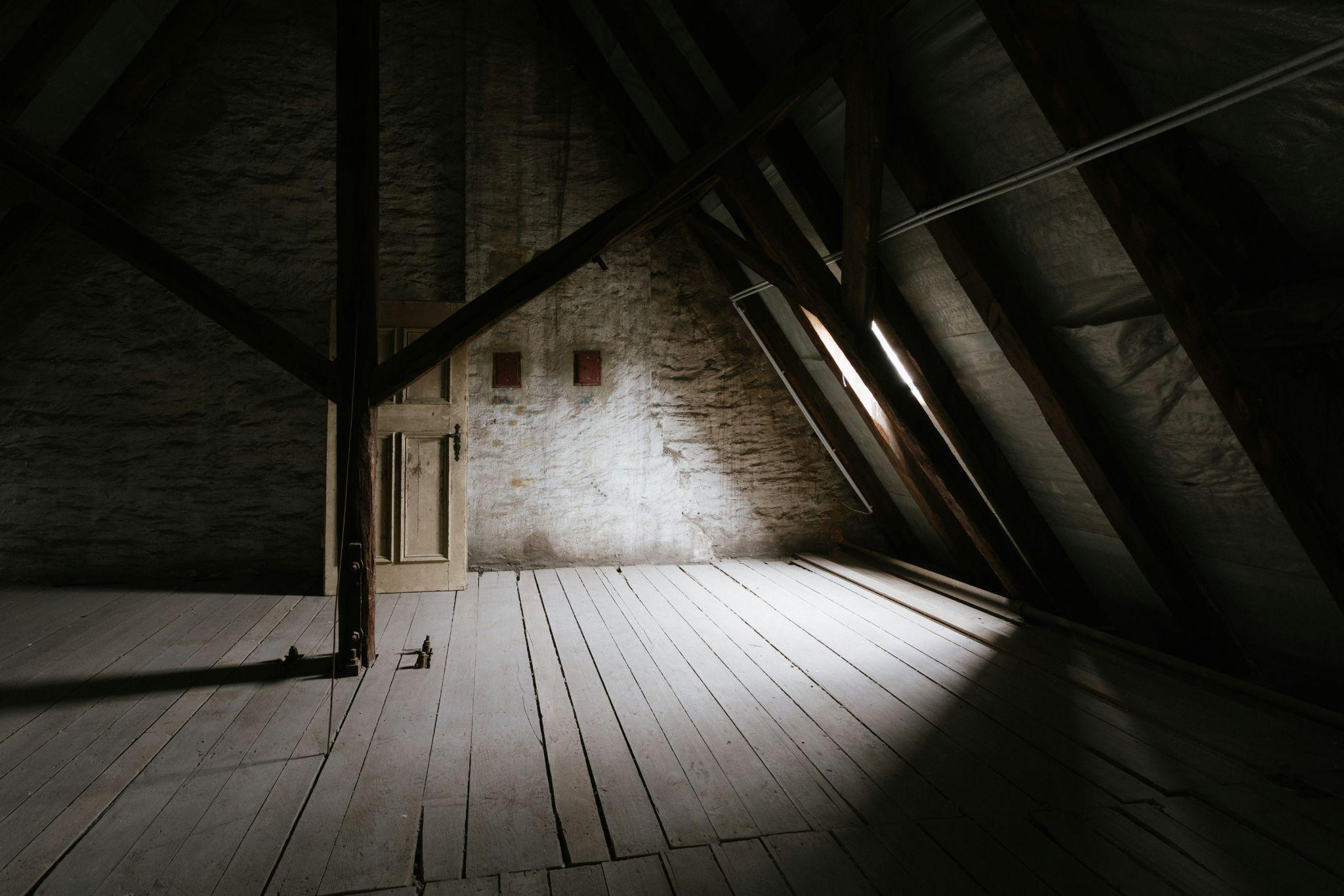 An unfinished attic with exposed beams and wooden flooring highlights the need for attic insulation in Fresno.