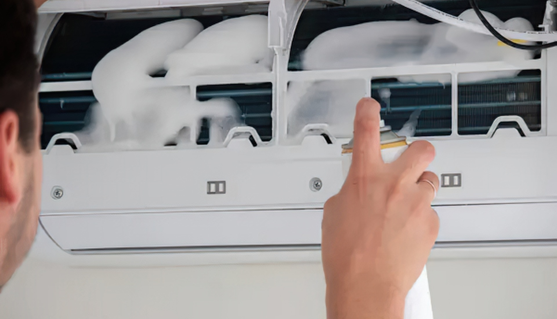 Person applying cleaning foam to the exposed coil of a wall-mounted indoor air conditioner
