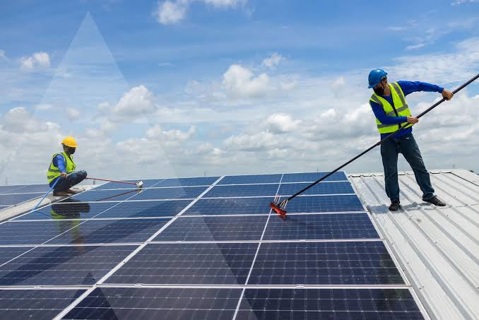 Technicians in safety gear cleaning rooftop solar panels