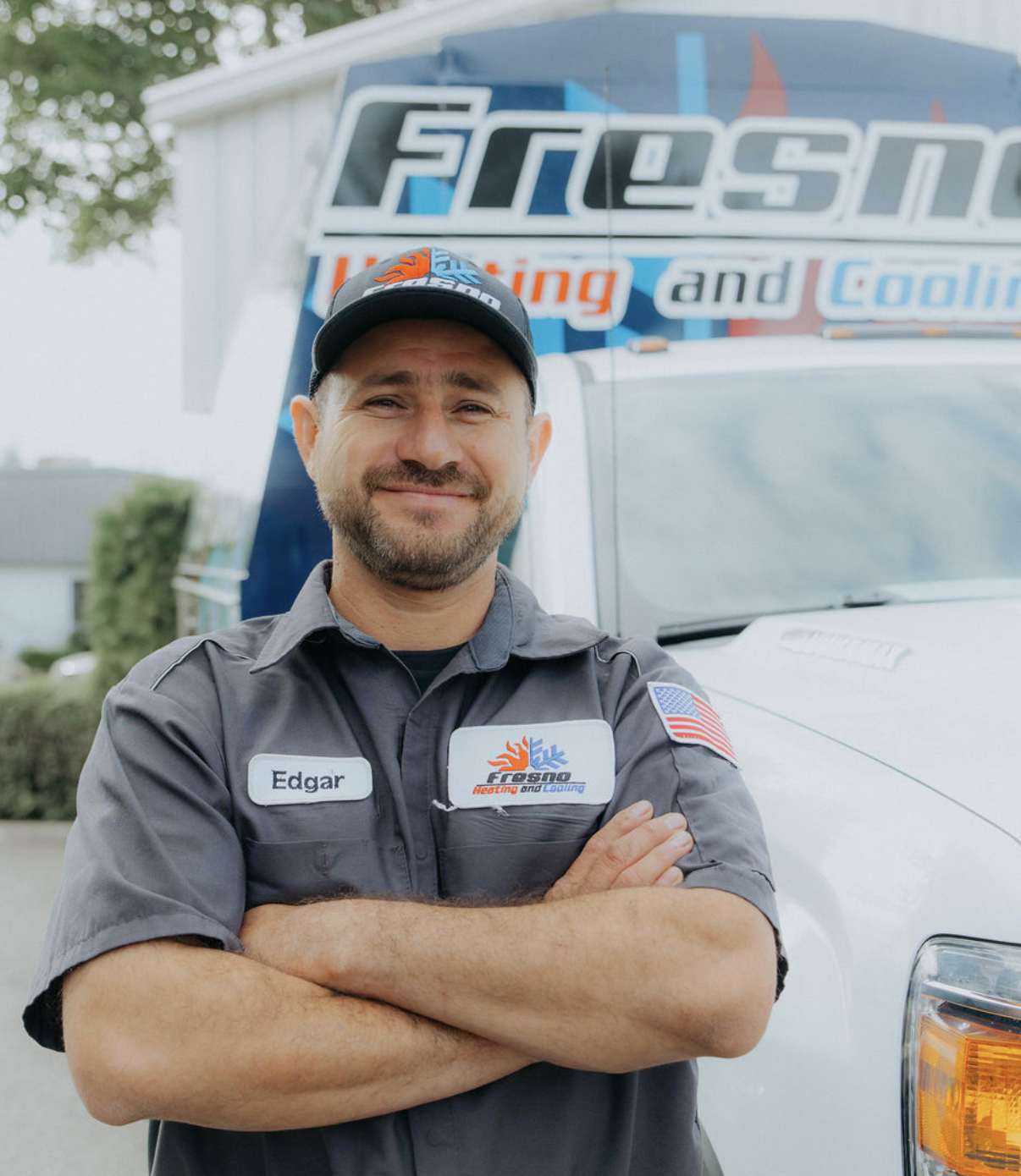Edgar, installer at Fresno Heating and Cooling, standing with arms crossed in front of a company service truck