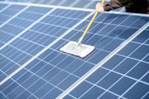 Person cleaning rooftop solar panels with a long-handled brush