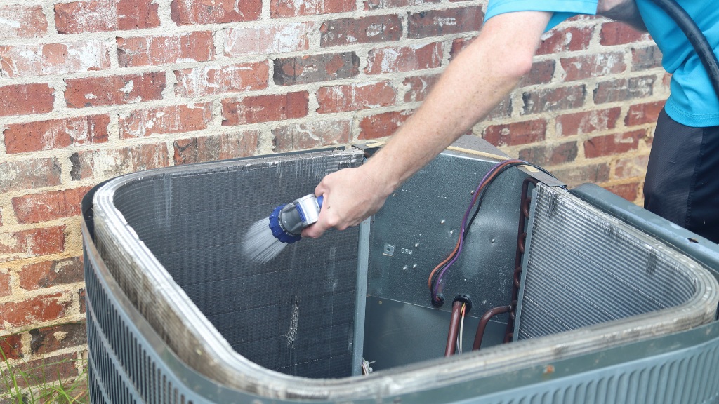 Technician cleaning the condenser coils on an outdoor air conditioning unit during a tune-up